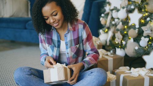 Free Smiling woman unwrapping a gift beside a decorated Christmas tree indoors. Stock Photo
