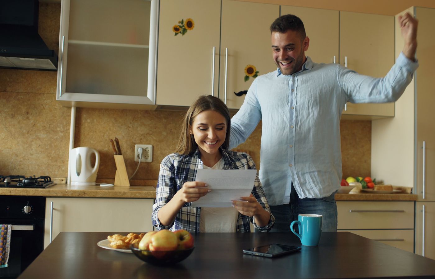 A joyful couple in a cozy kitchen, celebrating good news received by mail.
