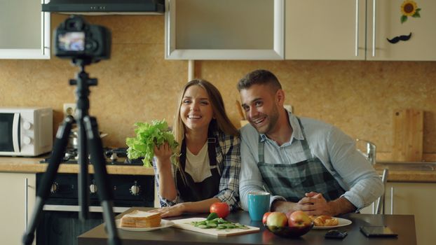 Couple filming a cooking video in a modern kitchen with fresh vegetables.