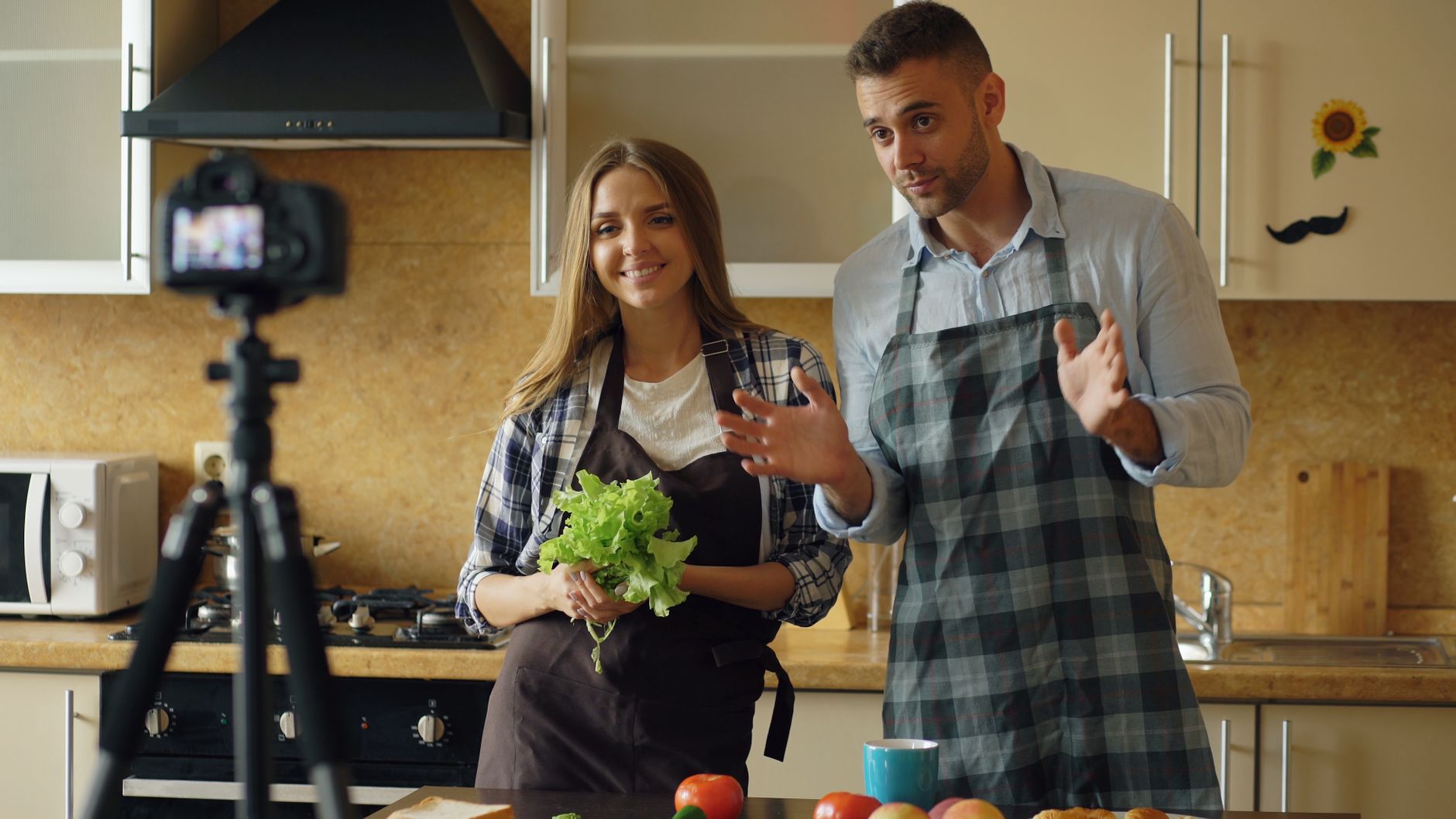 Young couple creating a cooking tutorial video in a modern kitchen setting.
