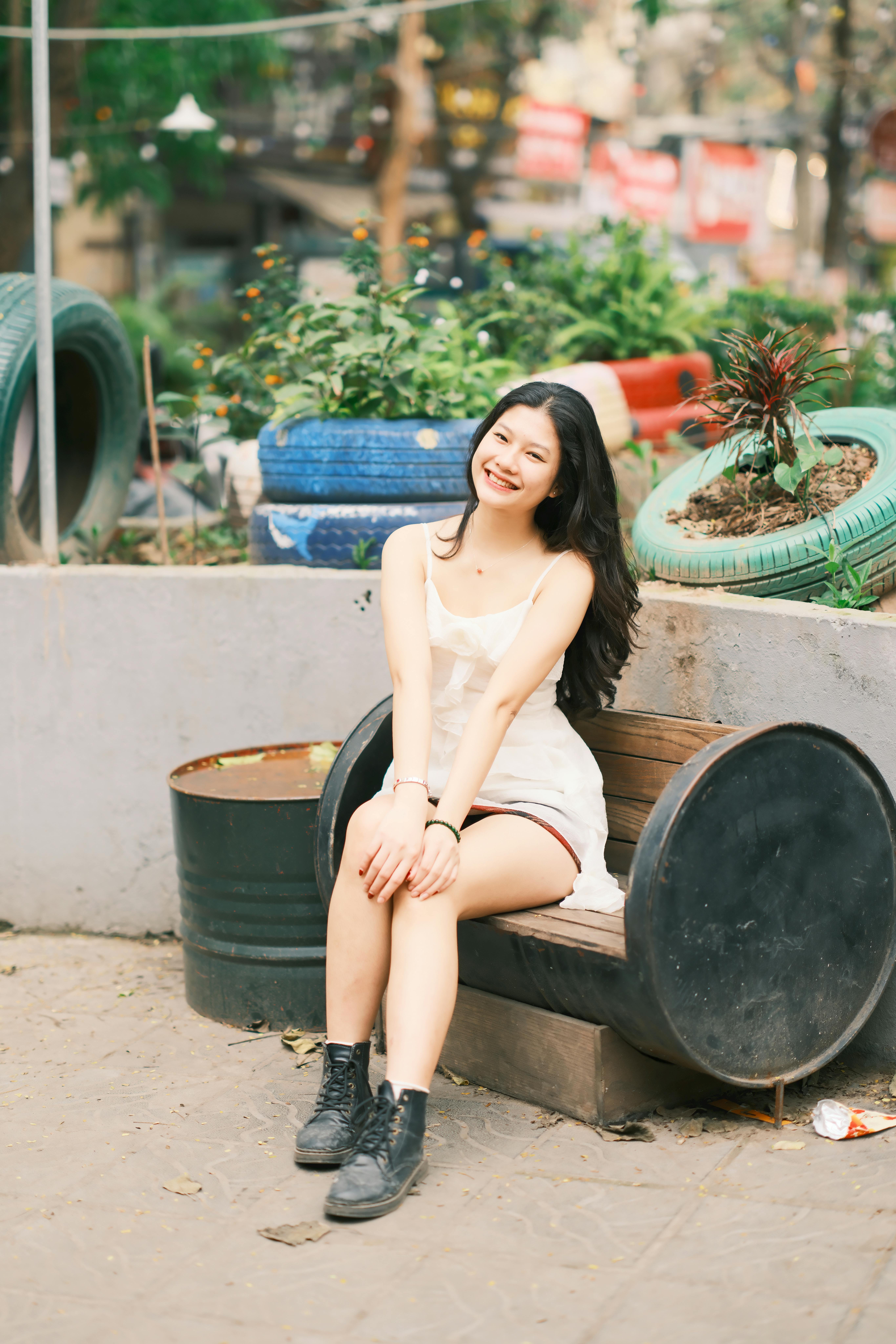 A young woman sits joyfully on a recycled tire bench in an outdoor park in Vietnam.