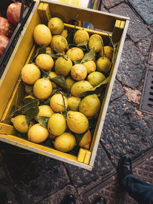 Free Ripe yellow lemons displayed in a wooden crate on a cobblestone street, showcasing a rustic appeal. Stock Photo