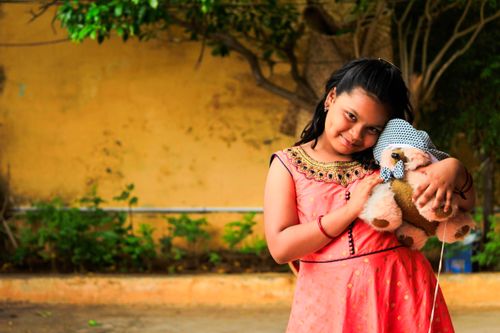 Free Smiling girl in pink dress lovingly embraces teddy bear in an outdoor garden setting. Stock Photo