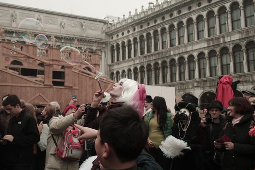A vibrant performer at the Venice Carnival entertains a crowd by blowing large bubbles.