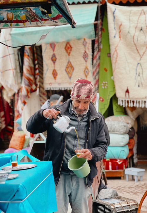 Free Local tea vendor pouring traditional Moroccan tea at the vibrant Marrakech Medina market. Stock Photo