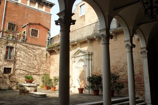 A tranquil Italian courtyard featuring classic architecture and potted plants under soft daylight.