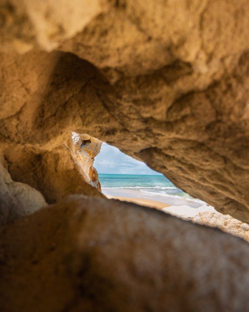 Free Captivating view of a serene beach as seen through a natural rock archway with turquoise waters and clear skies. Stock Photo