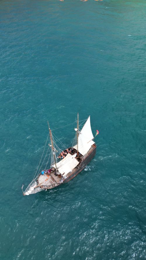 Free A historic sailing ship travels the clear blue waters of Algarve, Portugal's coast. View from above. Stock Photo