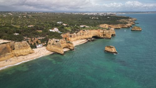 Free Breathtaking aerial shot of Algarve's dramatic cliffs and clear waters along the coast of Portugal. Stock Photo