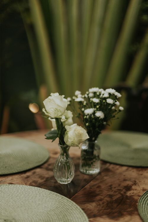Free A cozy dining table with white roses in vases, perfect for a romantic dinner setting. Stock Photo
