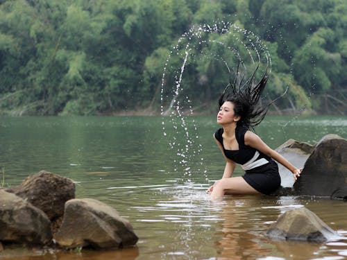 grátis Mulher Sentada Na Rocha Em Um Corpo D'água Foto profissional
