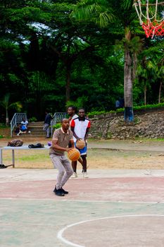 Three men enjoying a casual basketball game on an outdoor court surrounded by lush greenery.