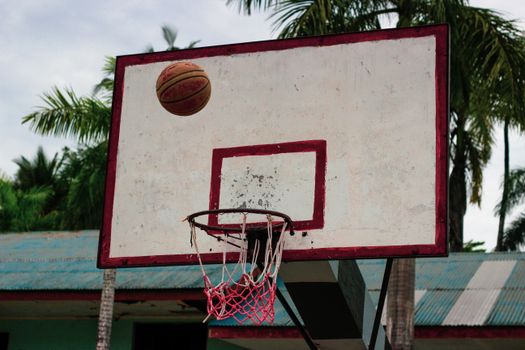 A basketball nearing a hoop on an outdoor court with palm trees in the background.