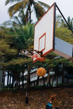 A basketball mid-flight to the hoop on a tropical outdoor court, surrounded by lush palm trees.
