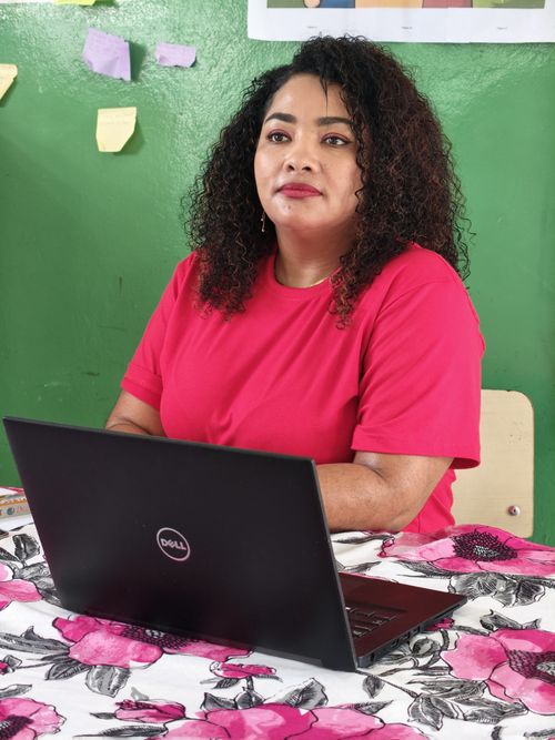 Free A woman in a red shirt sits confidently at a desk with a laptop, focused on her work in a vibrant office. Stock Photo