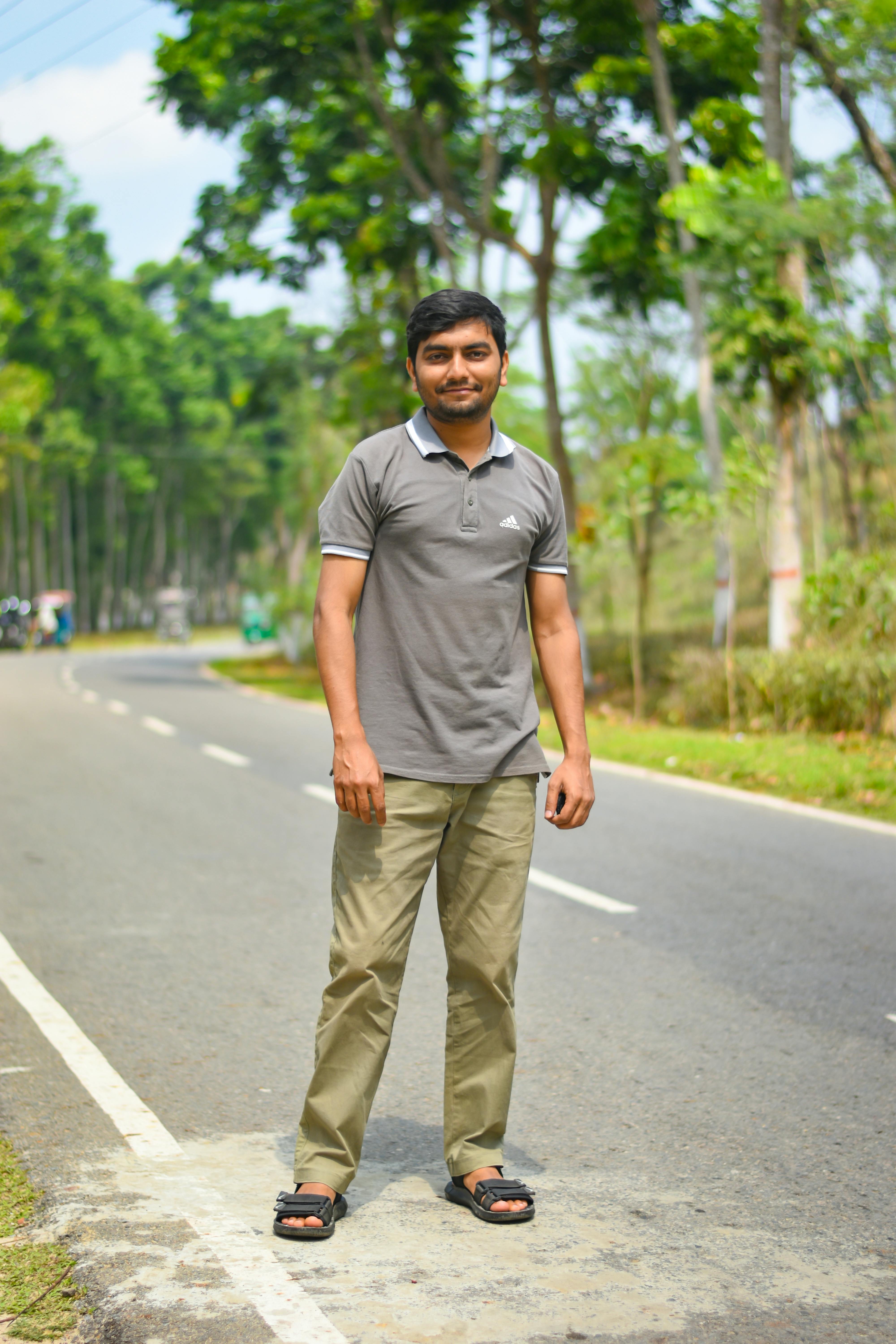 A man stands confidently on a quiet rural road surrounded by lush greenery in Sylhet, Bangladesh.