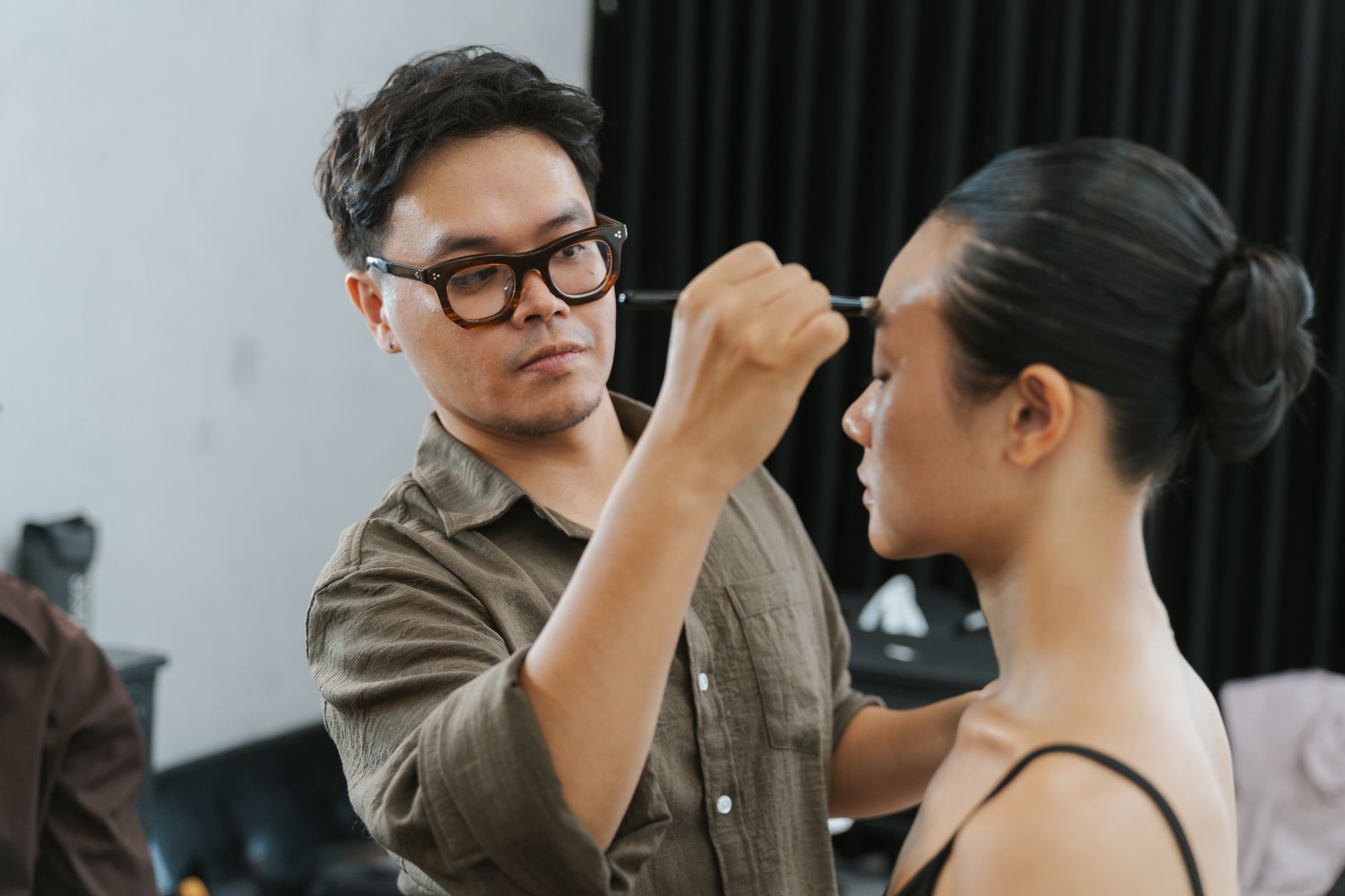 A makeup artist carefully applies makeup to a model in an indoor setting, showcasing professional styling.