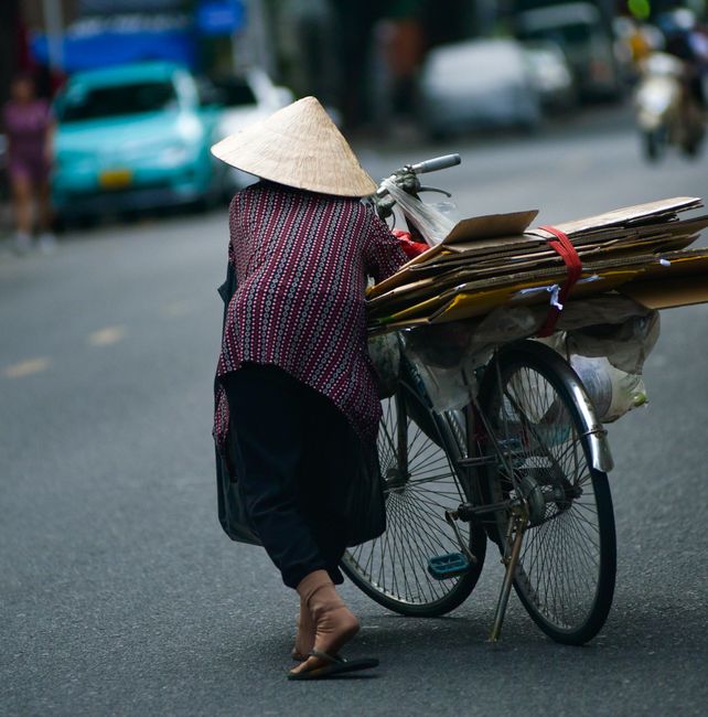 Adult woman wearing a traditional bamboo hat cycling on a busy street in Nha Trang, Vietnam.