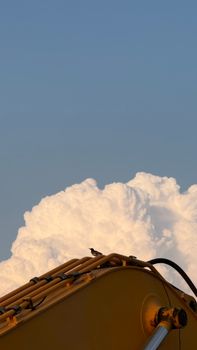 A bird on machinery set against dramatic cumulus clouds under a clear blue sky.