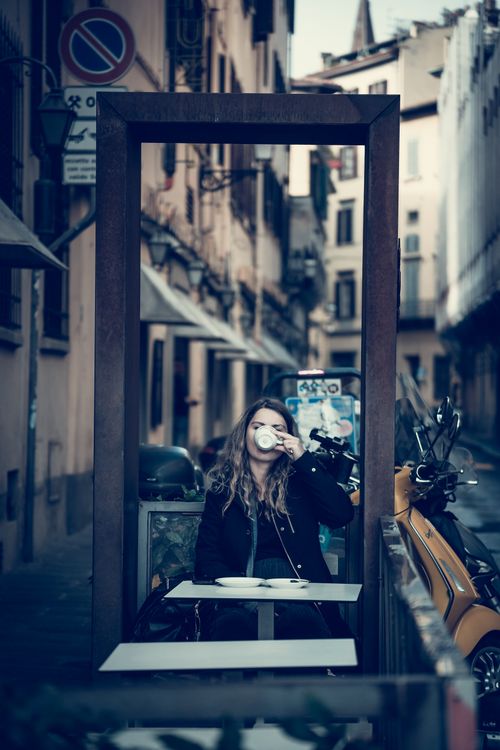 Free Woman enjoying a coffee in an outdoor street cafe in Florence, Italy, with a stylish urban backdrop. Stock Photo