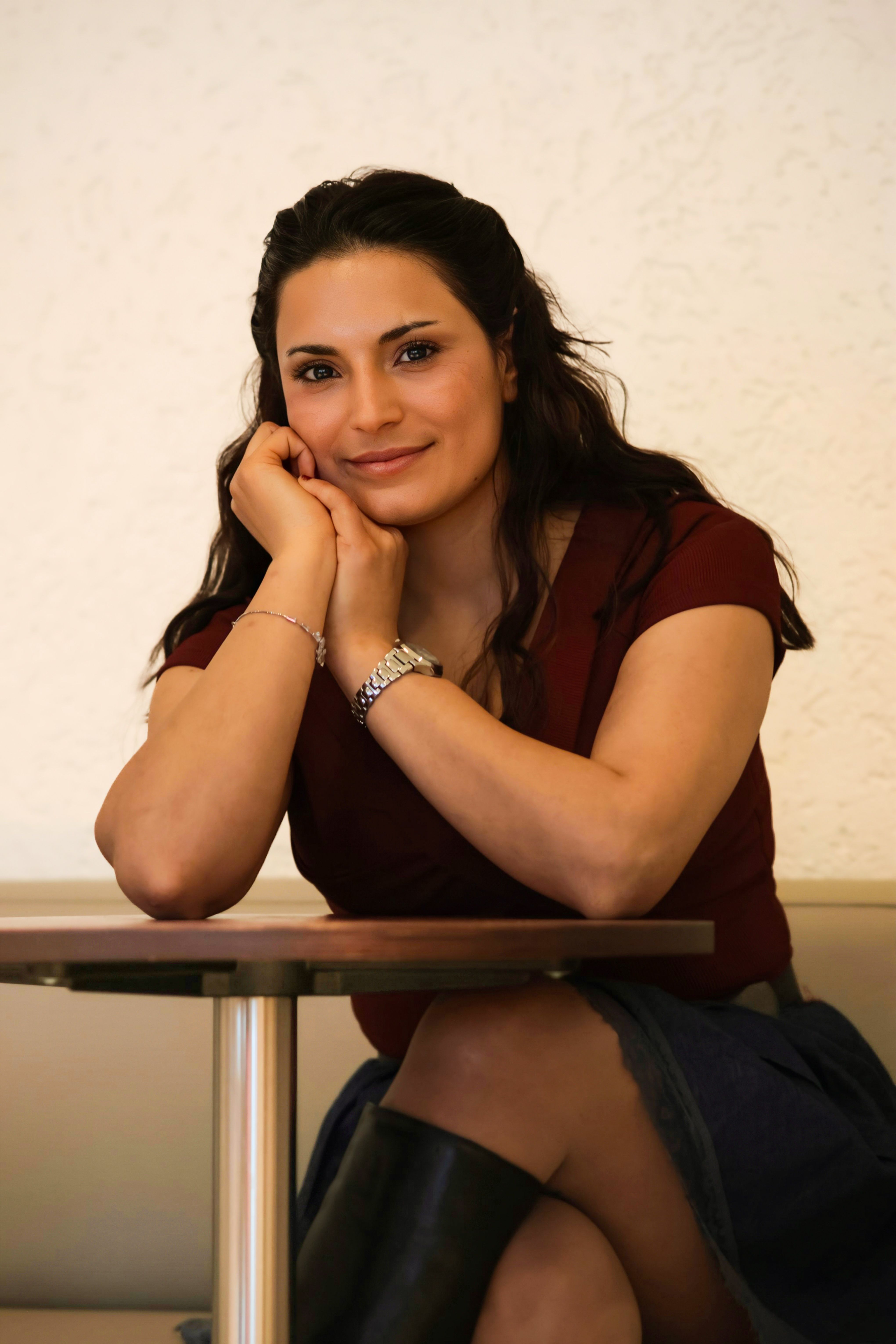 A woman in a relaxed pose sits at a table, exuding warmth and friendliness.