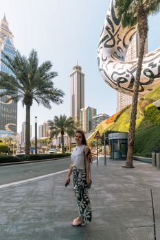 Woman stands amidst Dubai's futuristic architecture with palm-lined streets in the background.