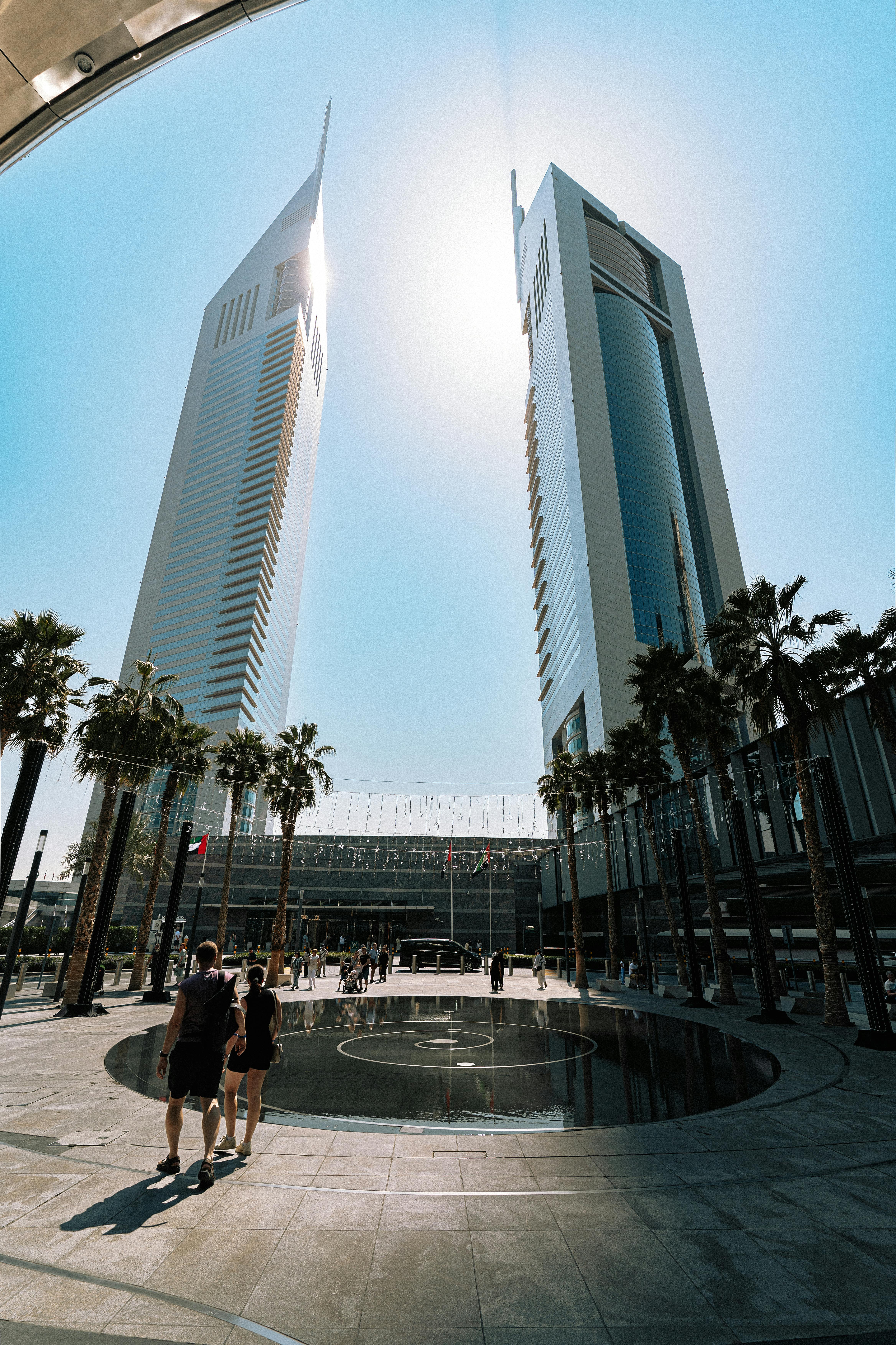 A vibrant daytime scene of the iconic Emirates Towers in Dubai, framed by palm trees under a bright sun.