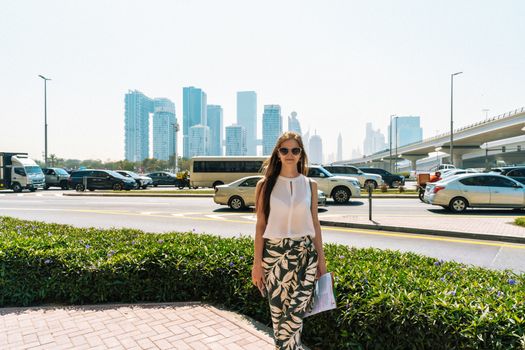 Stylish woman walking in Dubai with a view of the city's iconic skyline and bustling streets.