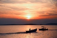 在平静的水面上宁静的日落期间，渔民在船上的剪影