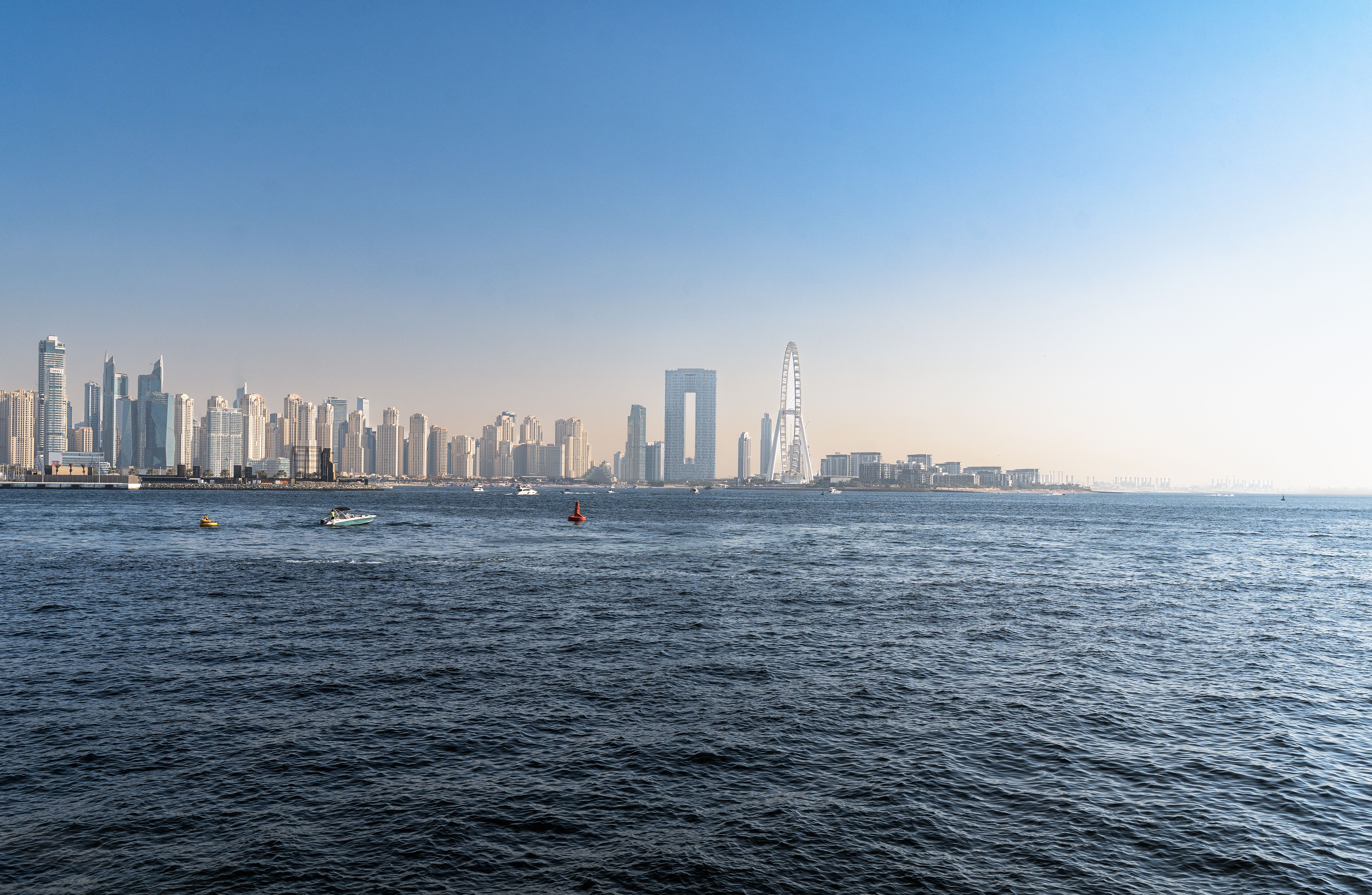 A stunning view of Dubai's skyline featuring skyscrapers, a Ferris wheel, and the vast sea under a clear blue sky.