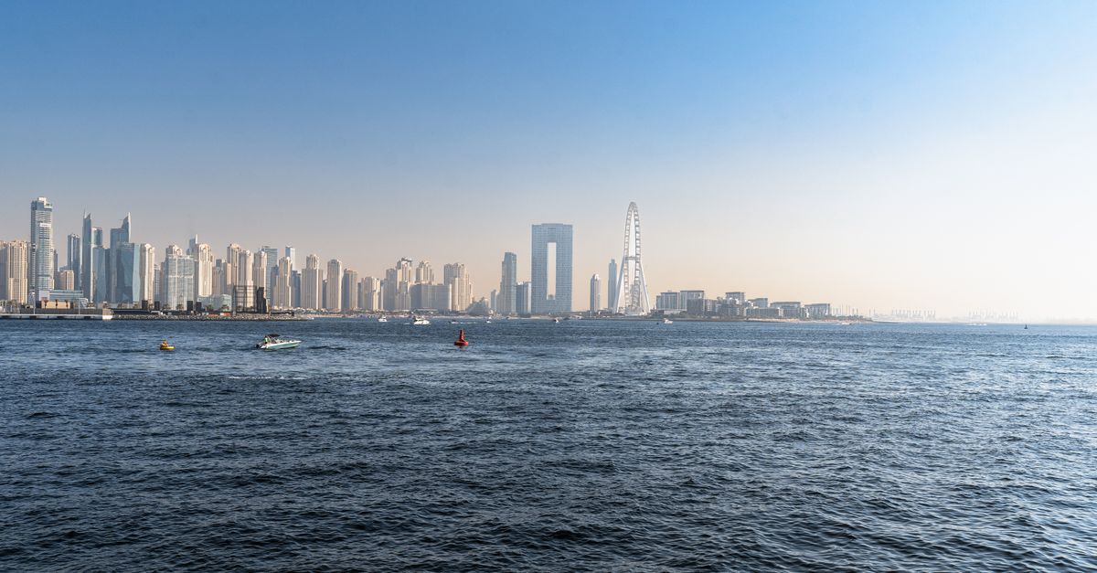 The silver geometric dome of Louvre Abu Dhabi glows against a clear sky above calm coastal waters.