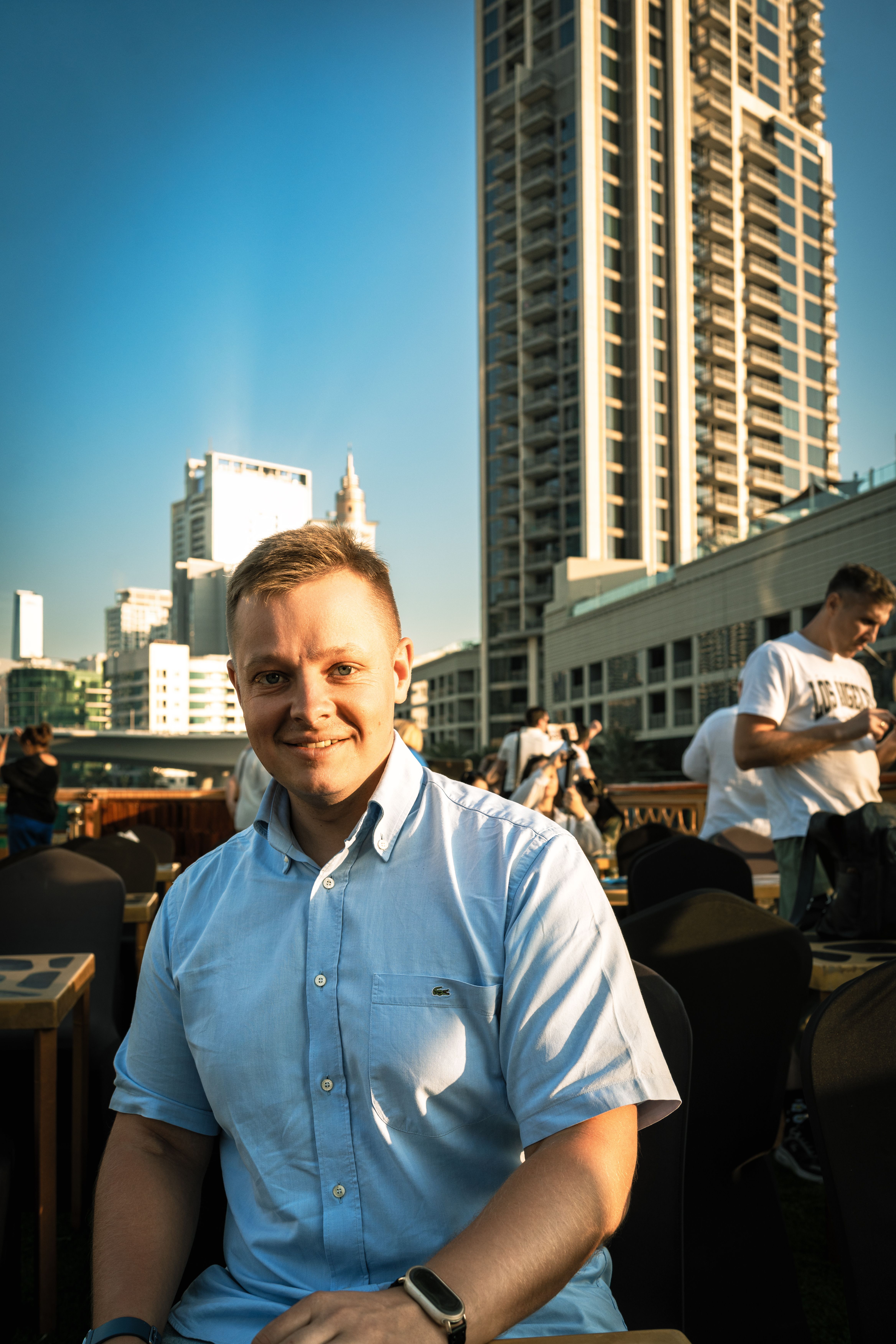 A man enjoying a sunny day at an outdoor cafe in Dubai with skyscrapers in the background.