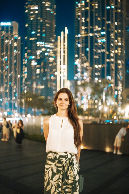 Free A woman stands in Dubai at night, beautifully illuminated by the vibrant city skyline. Stock Photo