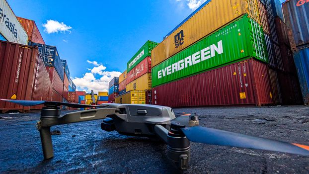 Drone on ground near colorful stacked shipping containers under bright blue sky.