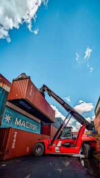 Red hydraulic crane handling shipping containers at a port under a clear blue sky.