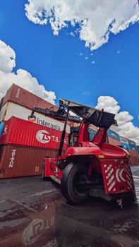 Dynamic view of a red forklift amidst stacked shipping containers under a vibrant blue sky.