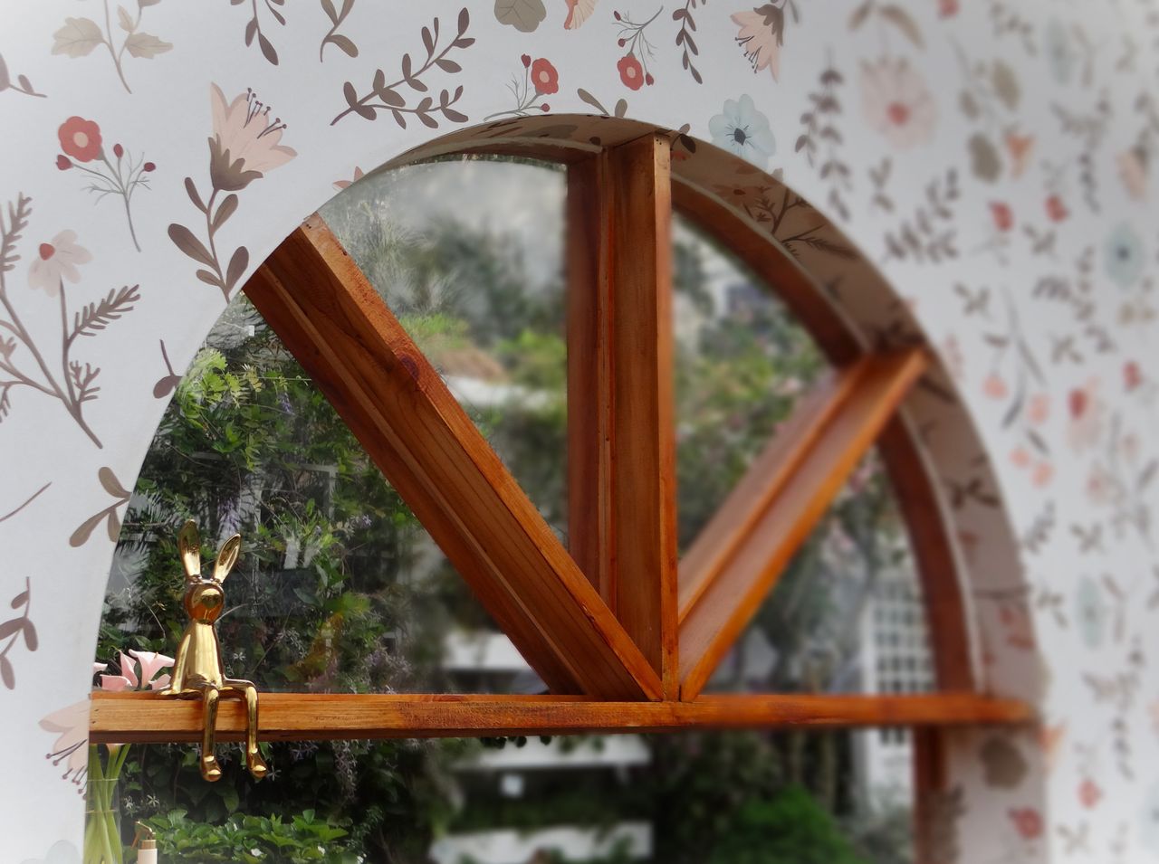 a wooden arched window with floral wallpaper and a small golden bunny
