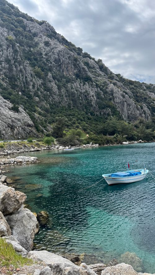 Free Tranquil water scene with a lone boat near rocky cliffs under a cloudy sky. Stock Photo