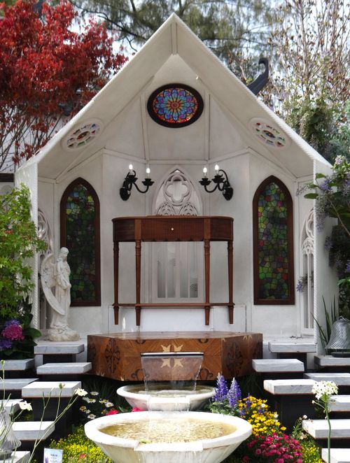 Free Stunning outdoor chapel with ornate stained glass windows and colorful flowers in a peaceful garden setting. Stock Photo