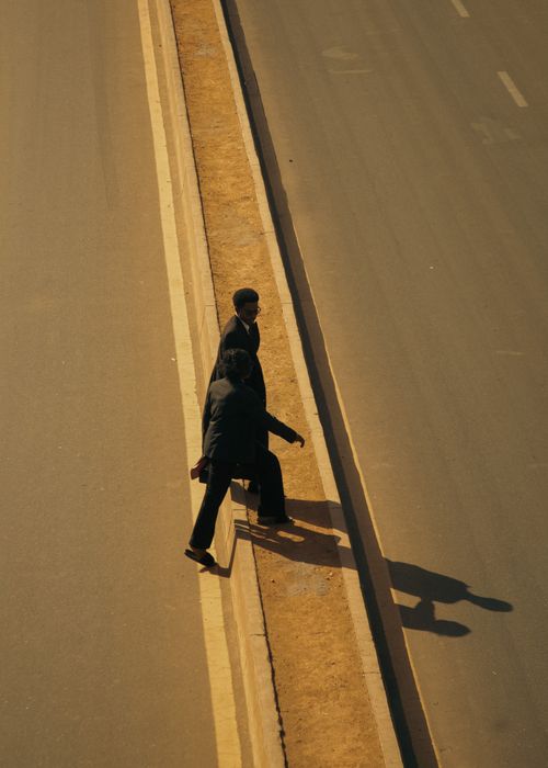 Free Top-down shot of two businessmen walking along a roadside, casting long shadows on a sunny day. Stock Photo