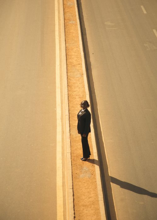 Free A solitary businesswoman stands on an empty road in a dramatic sunlit scene, highlighting isolation. Stock Photo