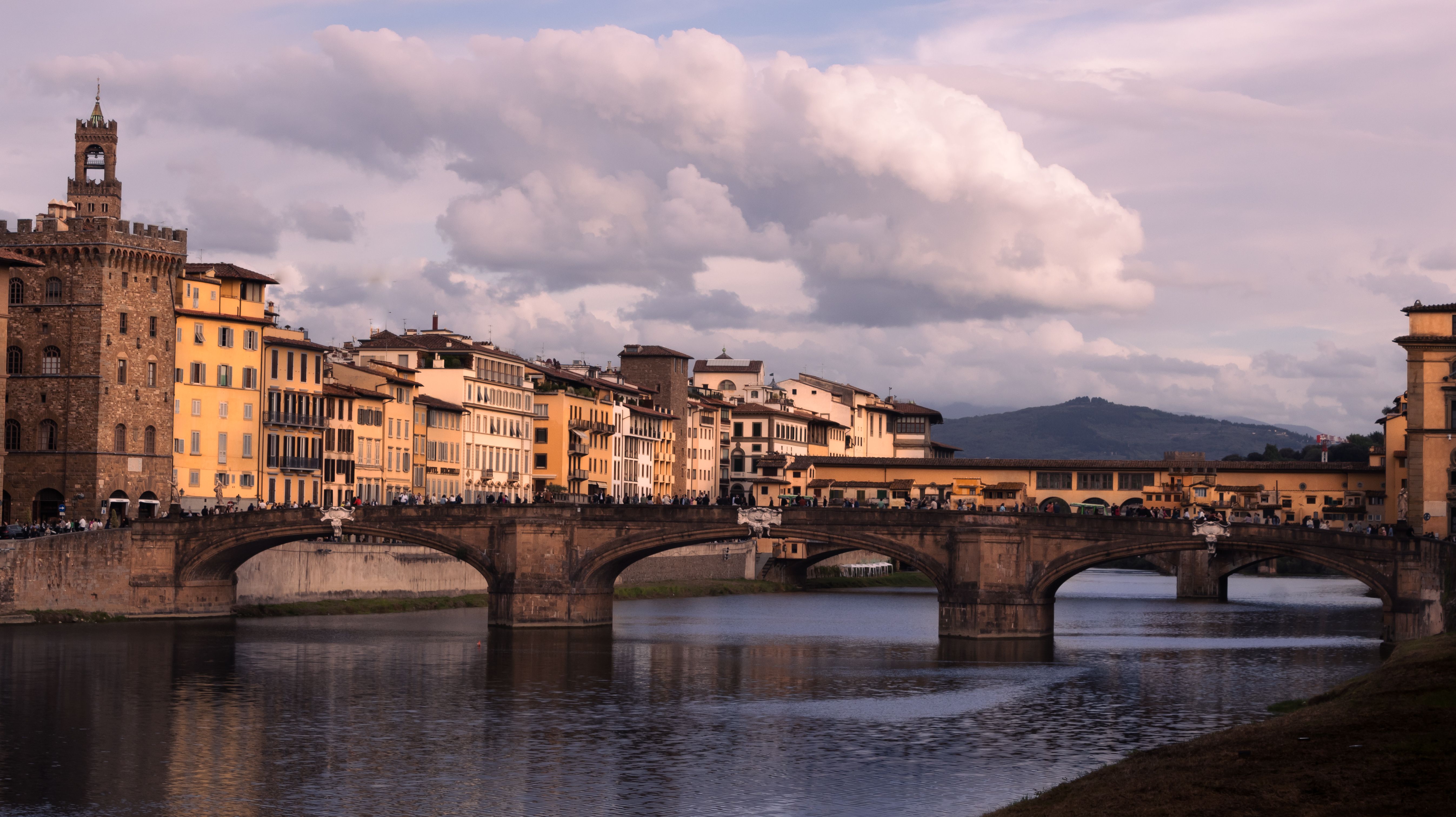 The historic Ponte Vecchio bridge spanning the Arno River in Florence, bustling with people during a bright April day.