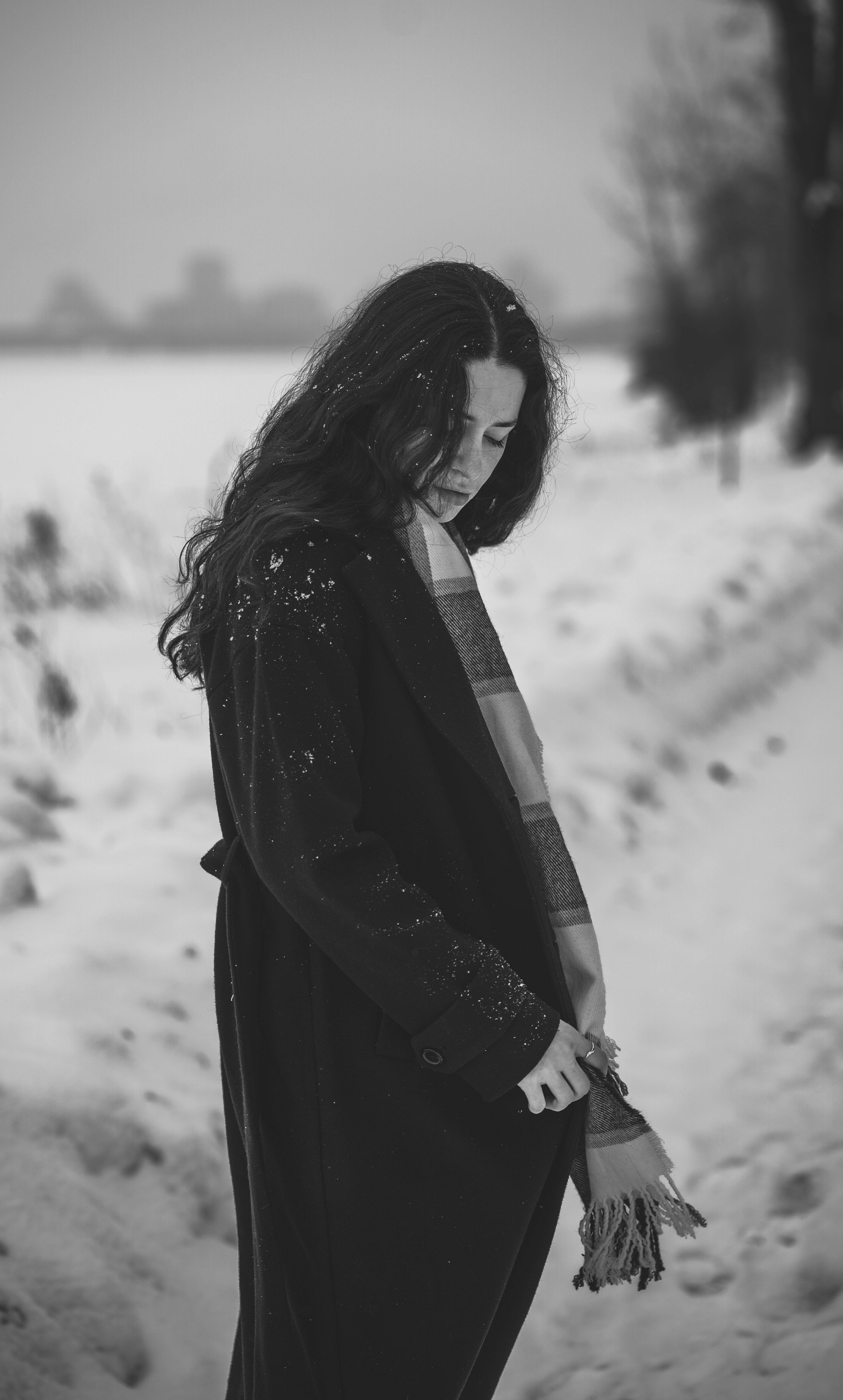 雪地背景下，一名穿着风衣的女子黑白肖像，展现了冬季时尚