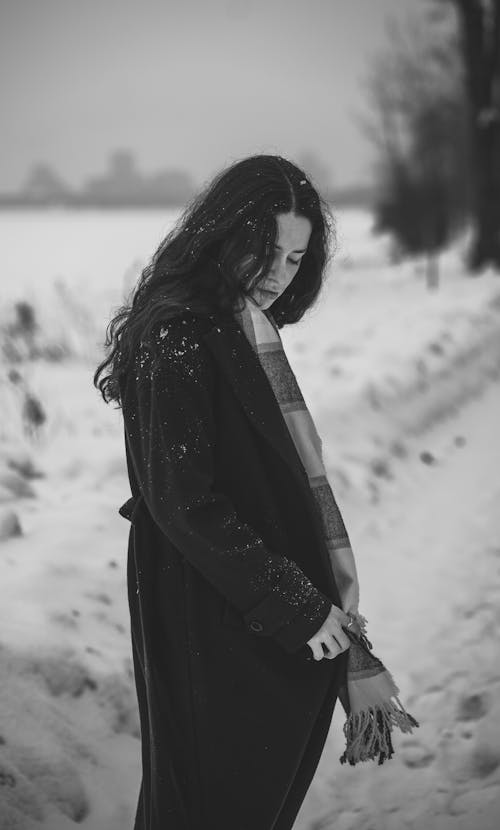 Gray scale Photo of Woman in Black Trench Coat Standing on Snow Covered Ground