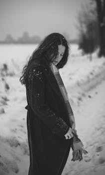 雪地背景下，一名穿着风衣的女子黑白肖像，展现了冬季时尚