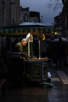 A street vendor sells produce under a canopy on a wet, rainy evening in an urban area.
