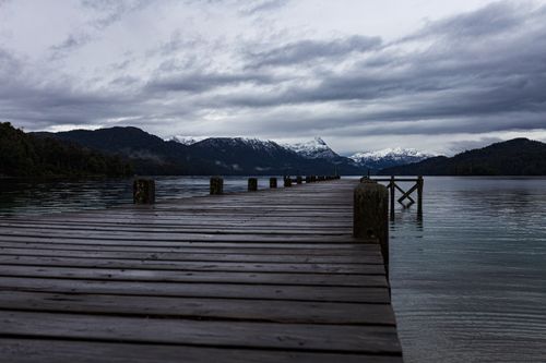 Free Serene view of a wooden dock on a lake with snowy mountains in the background. Stock Photo