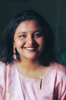 A woman in Dhaka wearing a light pink traditional dress, smiling warmly at the camera.