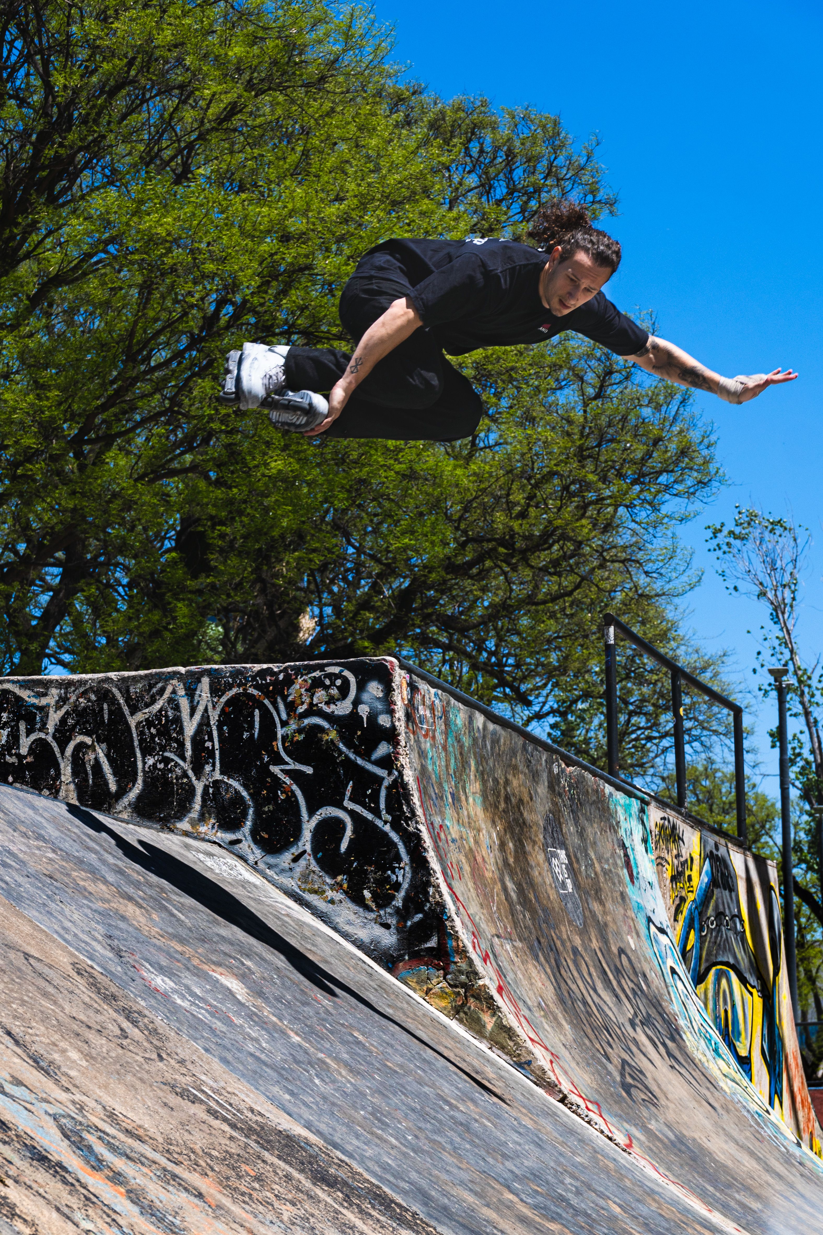 Skateboarder performing a jump at a skate park in Buenos Aires under a clear blue sky.