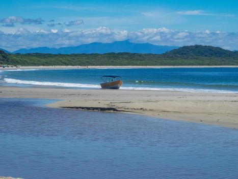 A solitary boat rests on a tranquil beach with lush hills and a vibrant blue sea.
